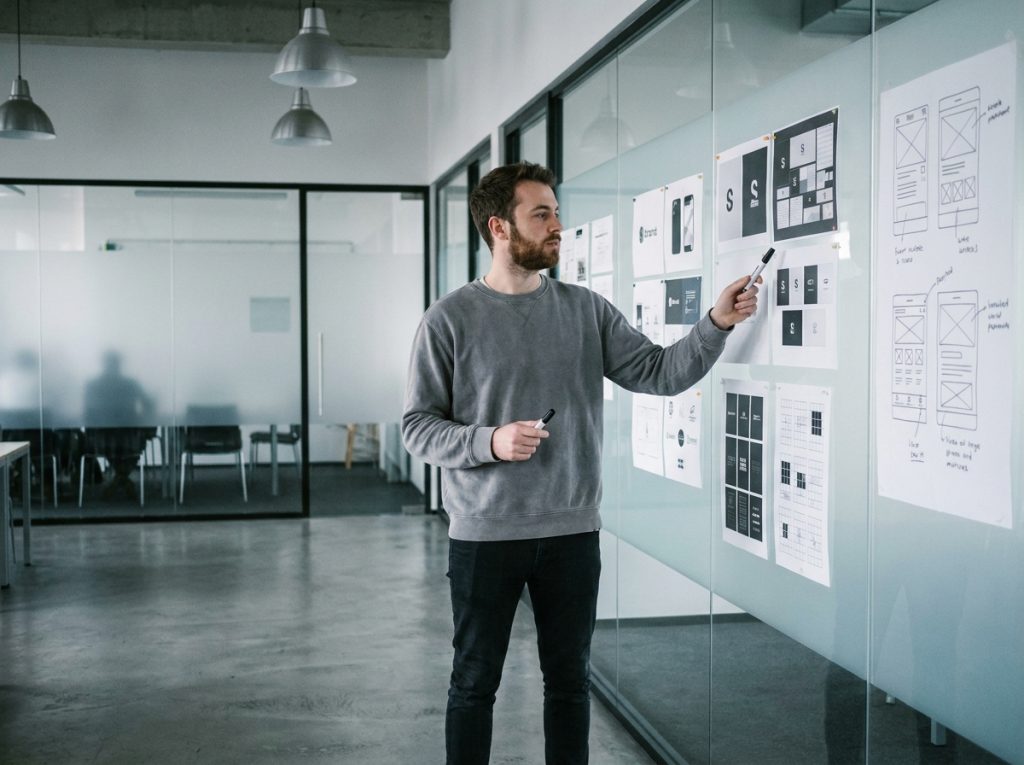Étudiant en master design évaluant des projets d'identité visuelle affichés sur un mur de critique en école de design